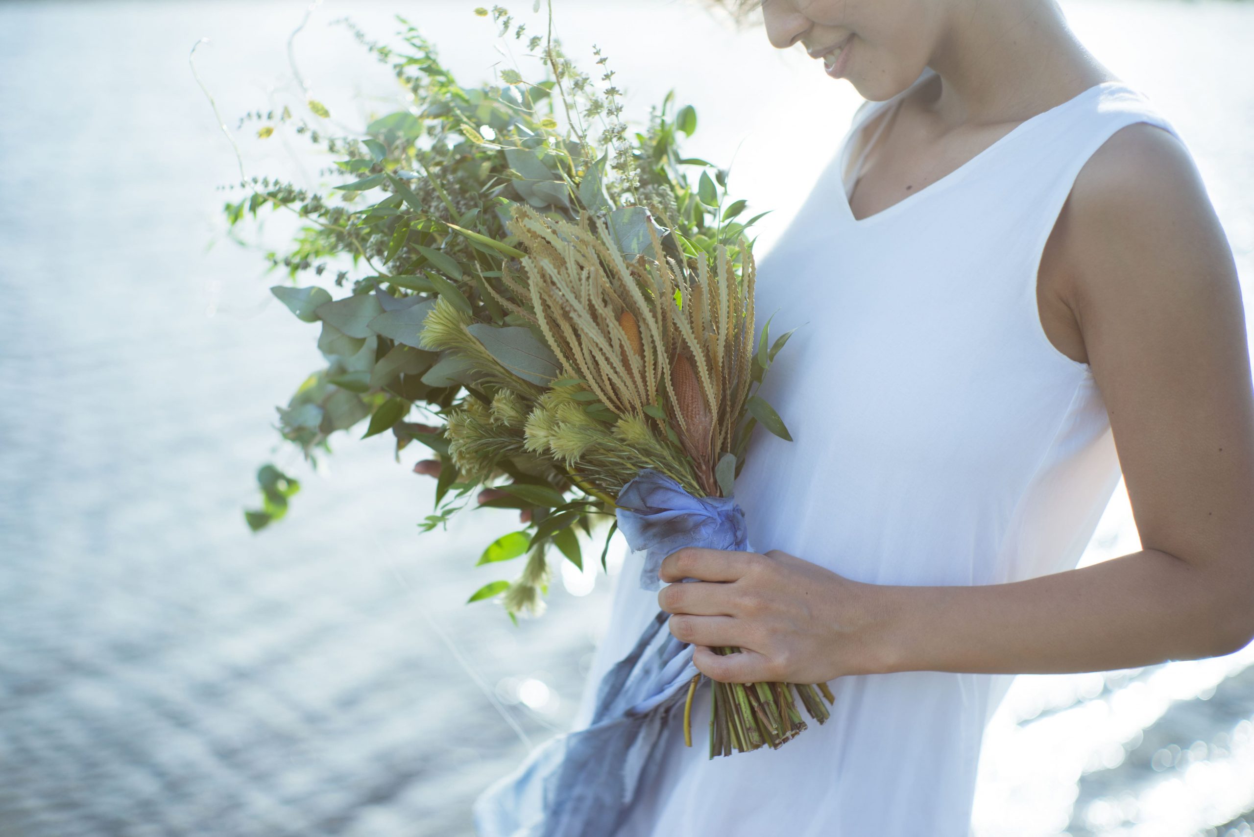光輝く沖縄の海をバックにウェディングブーケを持つ花嫁