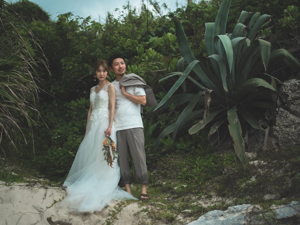 沖縄のビーチでグリーンをバックにした前撮り写真。